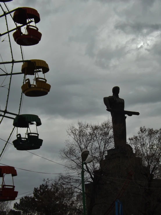 a statue next to an old ferris wheel in the sky