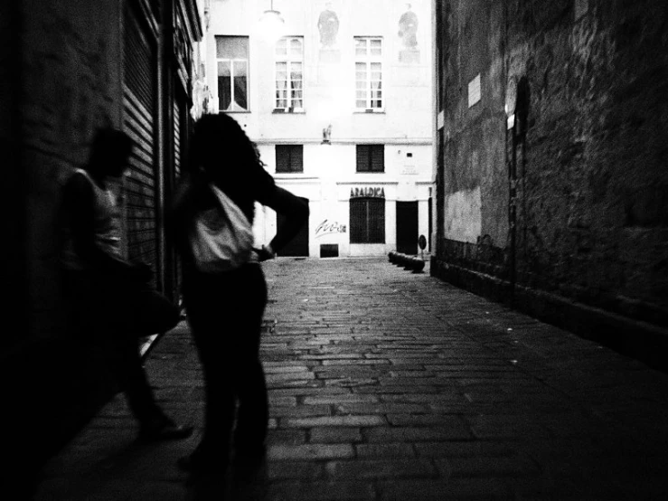 two people walking down an alley with a building in the background