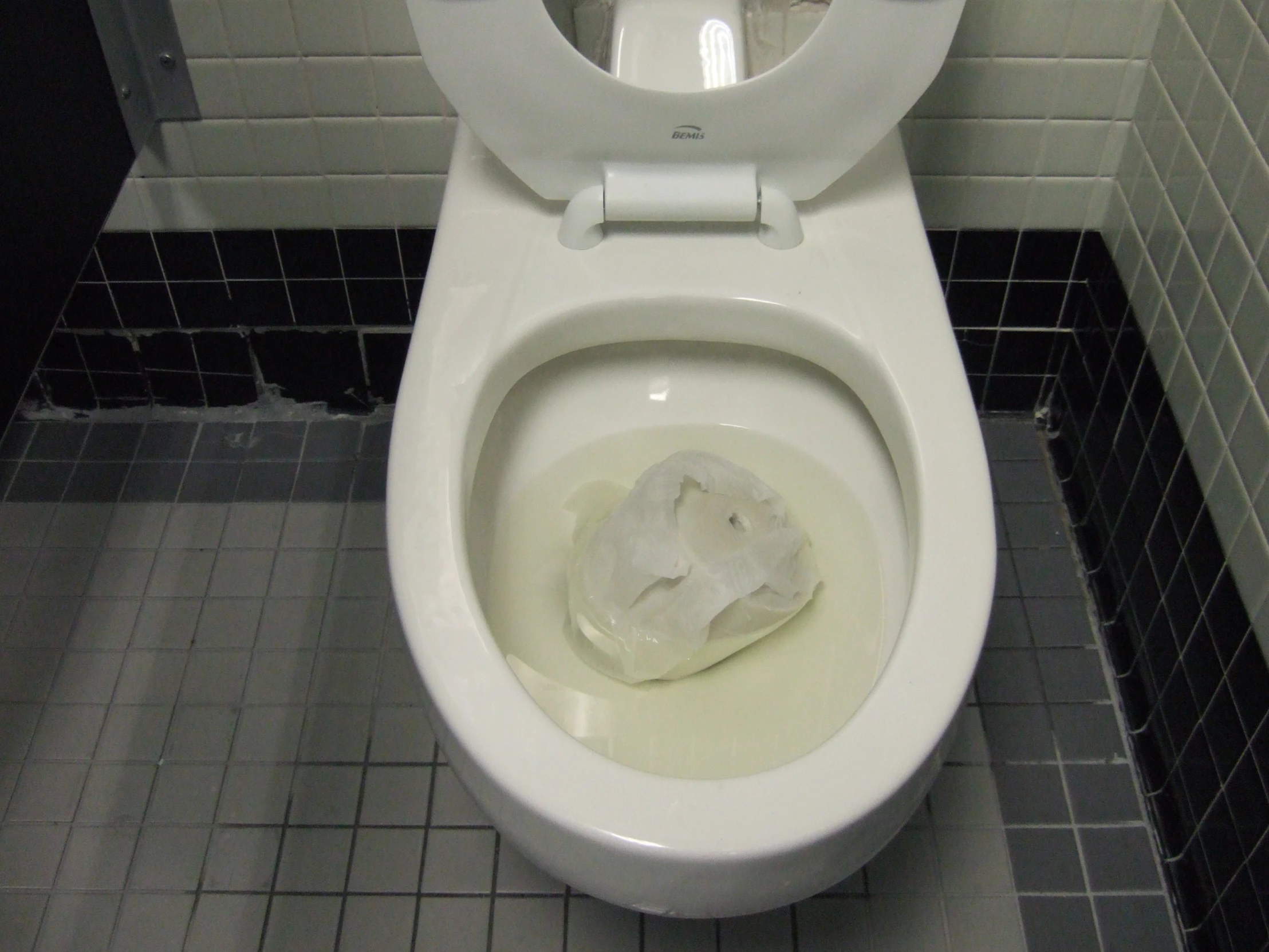 toilet with waste bag in middle with tile floor