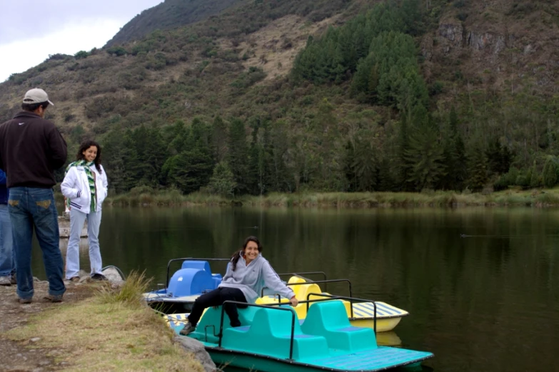 several people stand on a dock, one sitting on a pedal boat