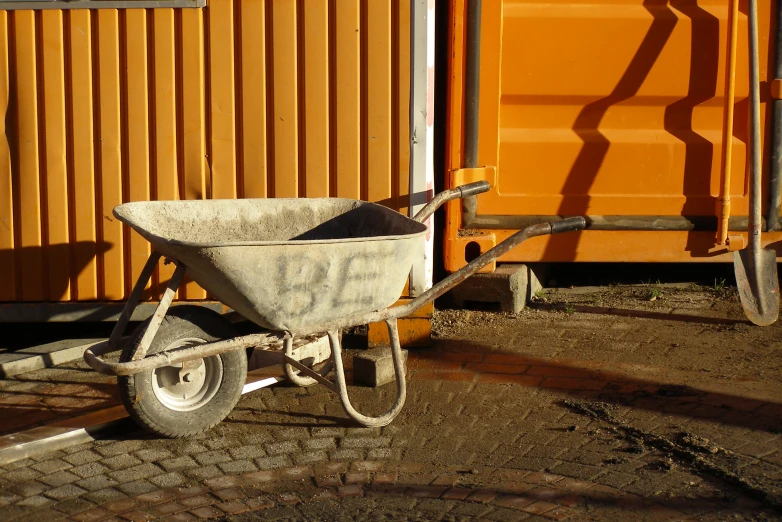 an old wheel barrow next to orange shipping containers