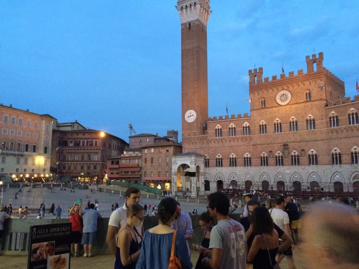 several people are standing in front of buildings at dusk