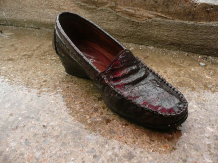 a man's brown shoe with red trim sitting on cement