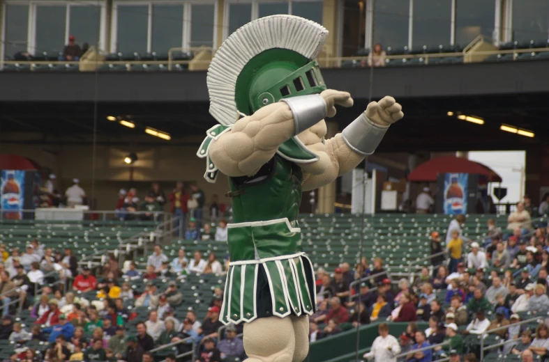 mascot in green and white uniform performing at baseball game