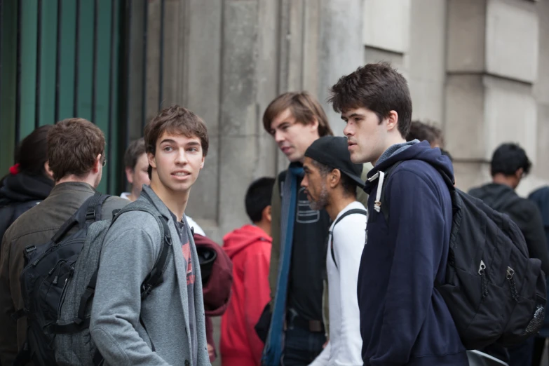 three young men are standing on a sidewalk, and one man has his eyes open