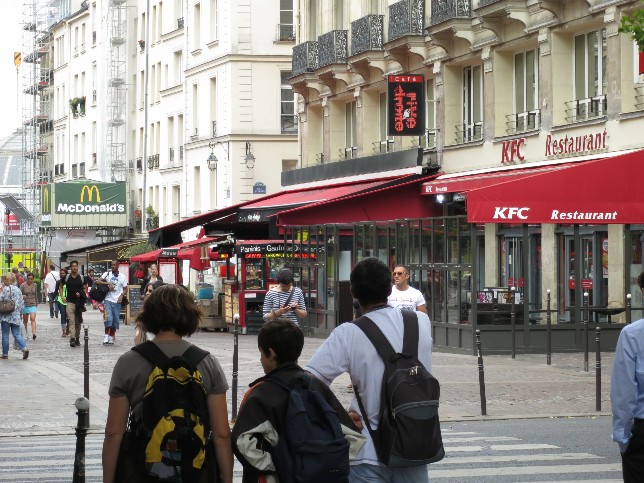 pedestrians walk through a downtown sidewalk that is lined with restaurants