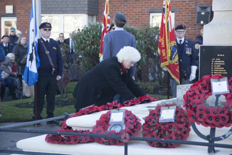 woman laying wreaths on a plaque near a group of uniformed men