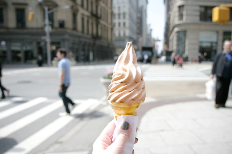 a hand is holding up a yellow gelato on a city street