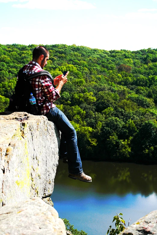 a man that is sitting on a rock with a phone