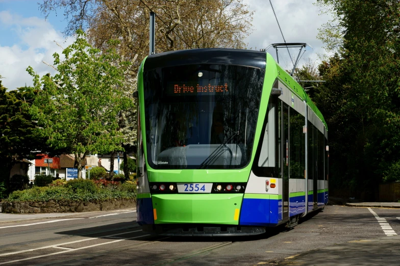 a green and white train passing by trees and a street