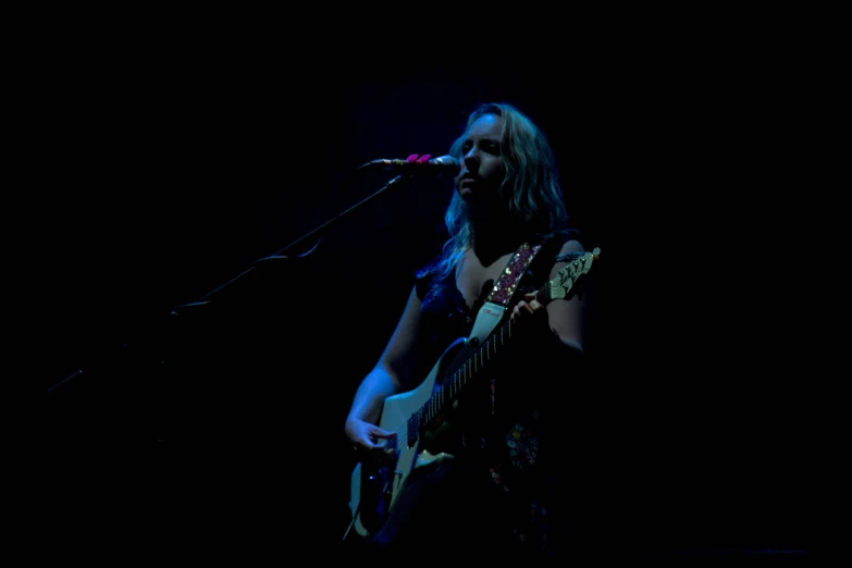 a woman playing guitar and singing into a microphone