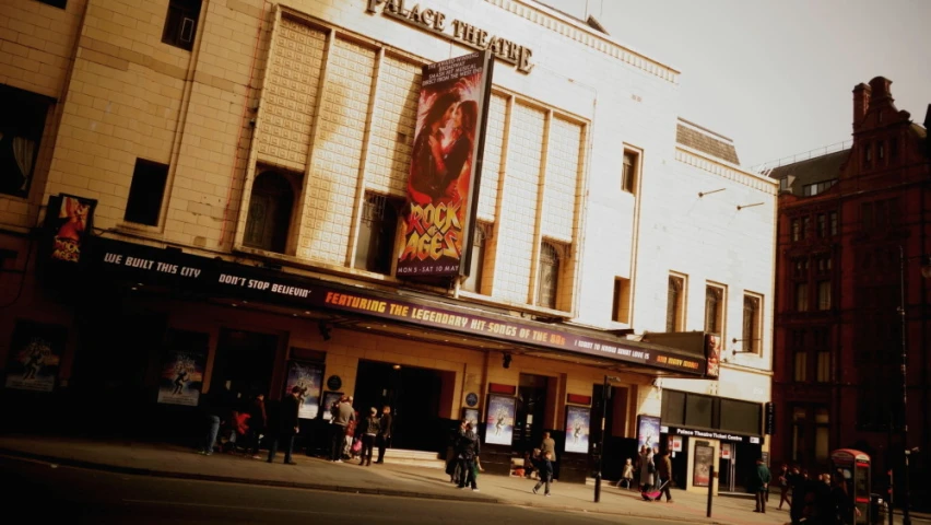 a group of people are gathered on the street in front of a theatre