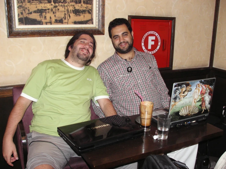 two men sitting together at a table and drinking some beverage