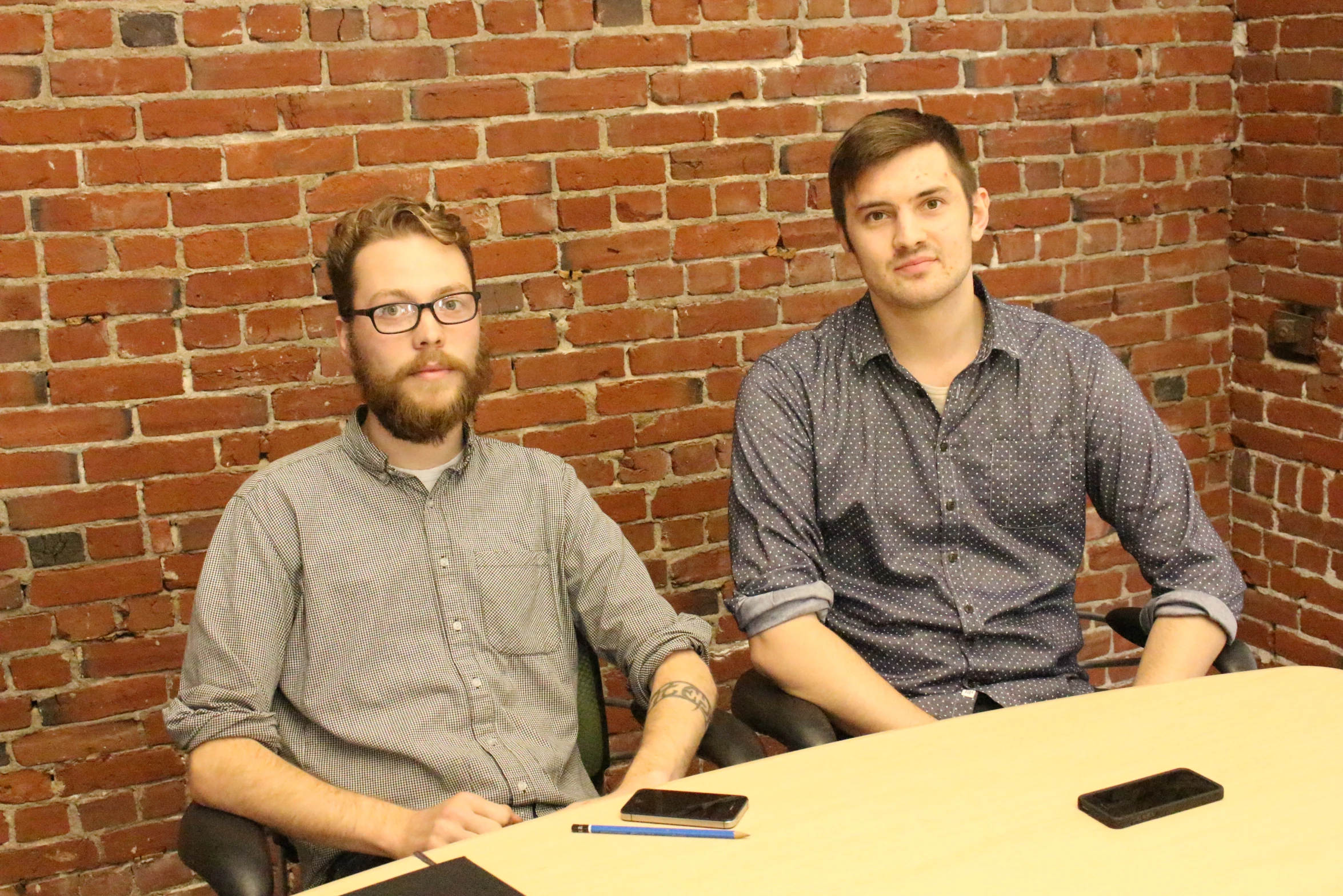 two men sitting at a table near a red brick wall