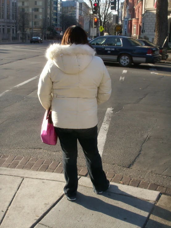 a person in a puffy jacket standing on the side of the road with a purple purse