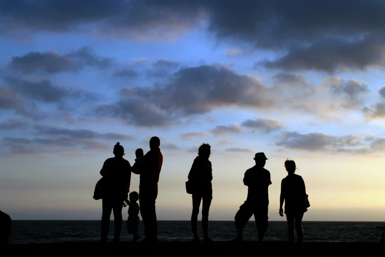 a group of people stand in silhouette in front of a body of water