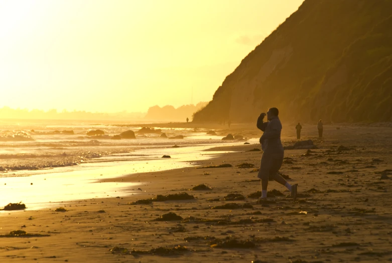 the man is walking on the beach while his cell phone is up to him