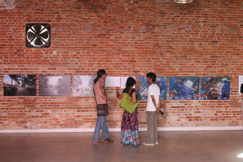 three people standing next to brick wall in front of art work