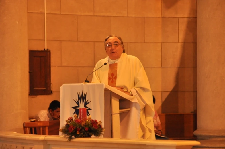 man speaking at podium in large building with white d