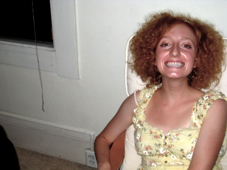 a girl with long red hair is smiling while sitting in a white chair