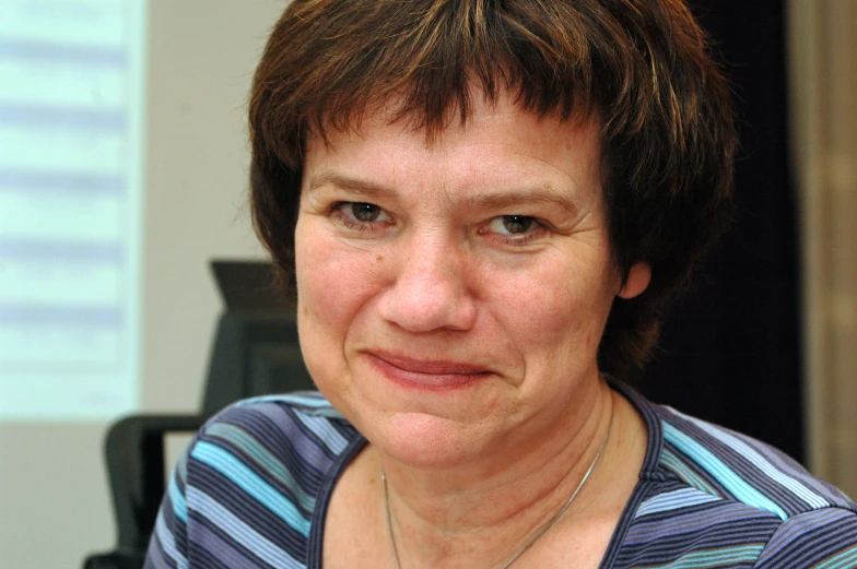 a woman with brown hair and wearing a blue striped top smiling