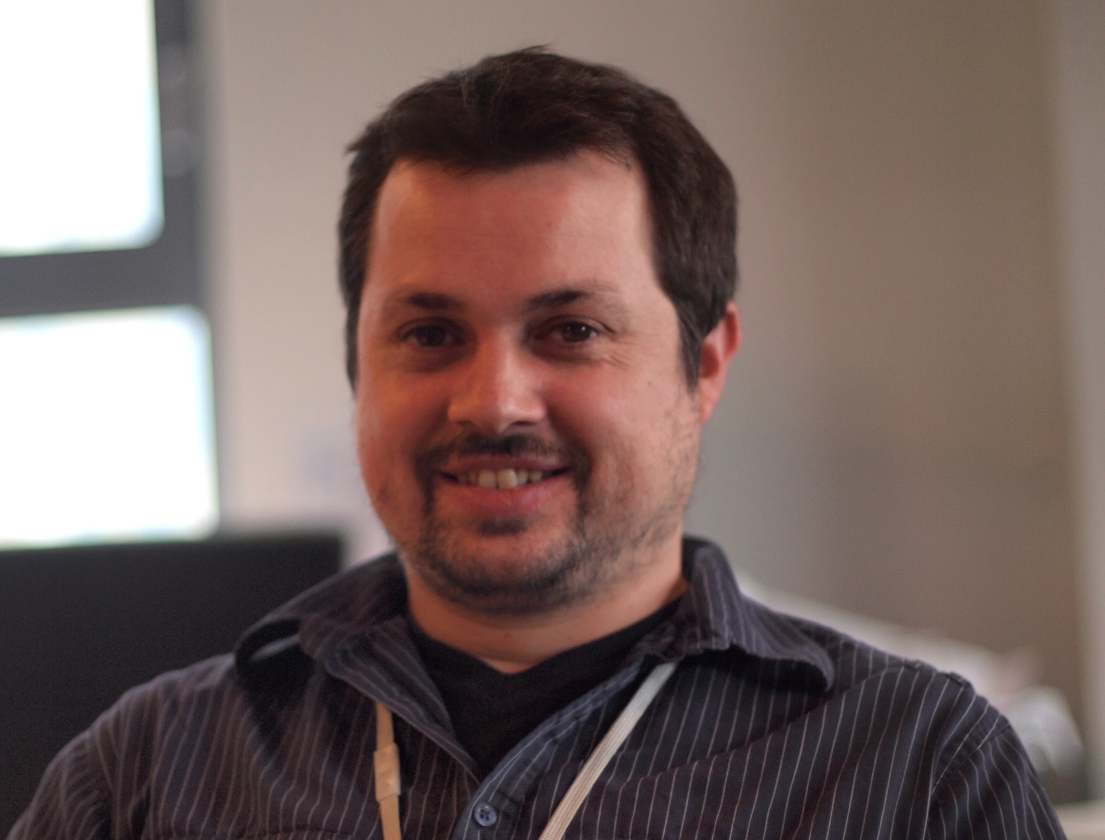 man wearing blue striped shirt smiling in front of window