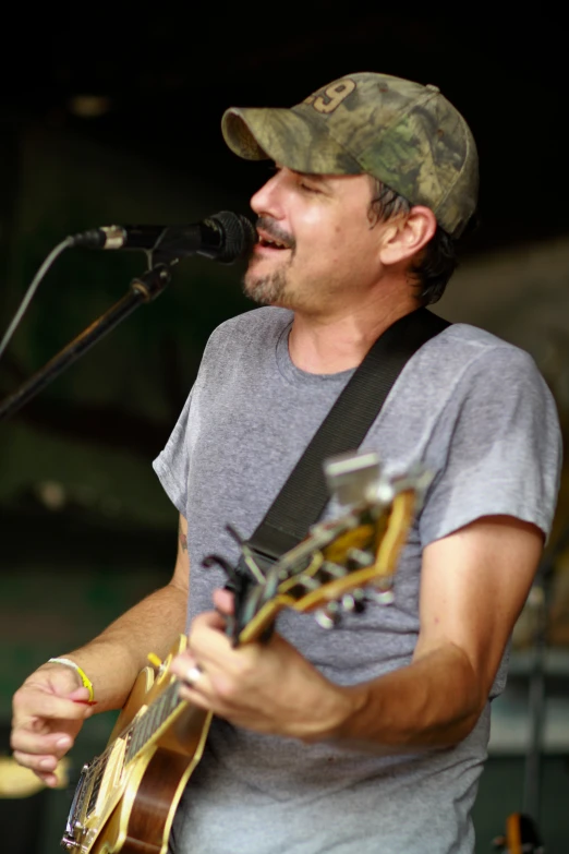 a male in a green and white cap and grey shirt is playing the guitar