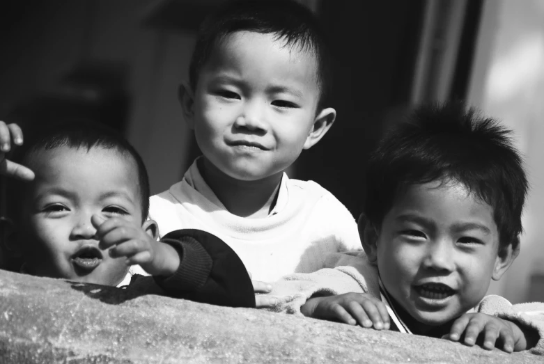 three young children stand on the ledge looking into the camera