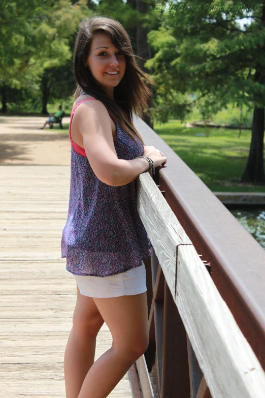 a pretty young lady standing by the edge of a wooden bridge