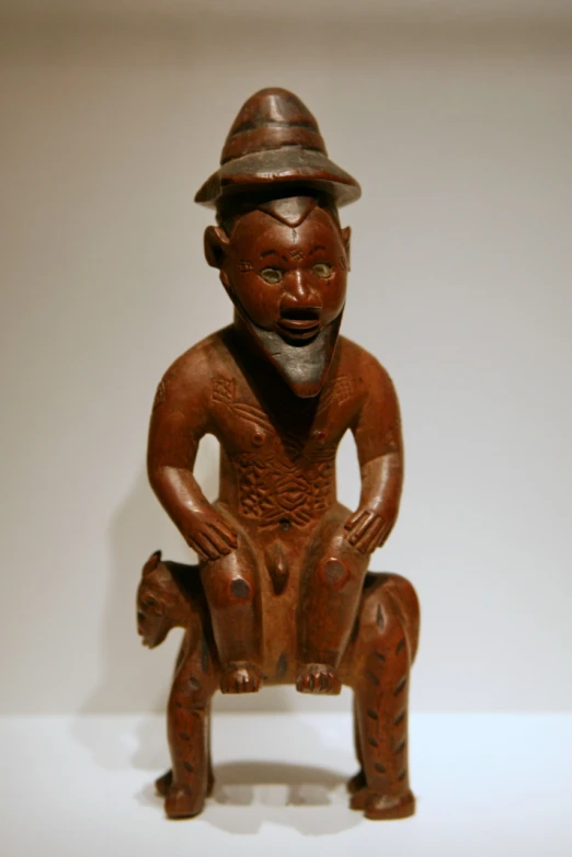 a wooden carved statue of a man wearing a hat sitting on a stool