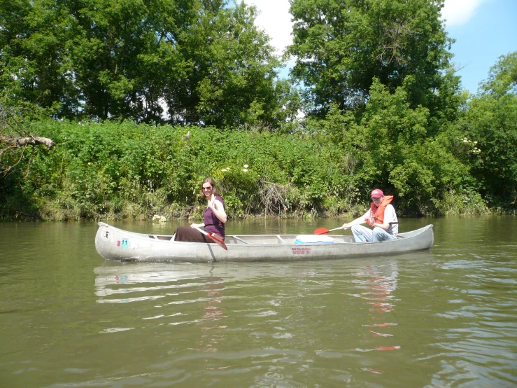 two people sit in a canoe, and paddle in the water