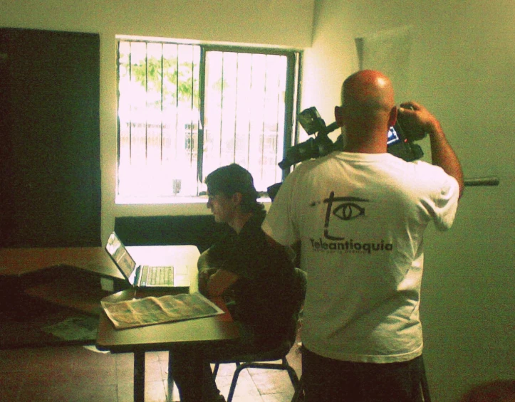 two men standing in a room with a desk and laptops