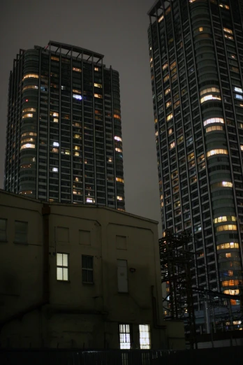 two tall buildings are at night with lights glowing