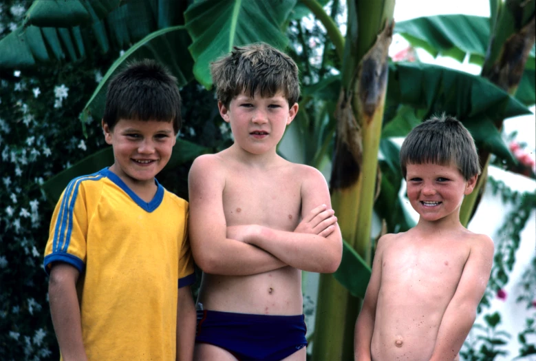 three boys posing with their arms crossed and a banana tree in the background