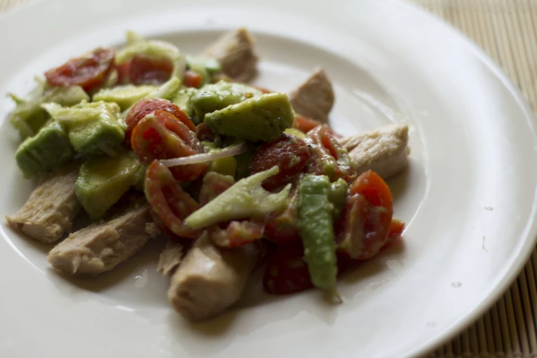 a white plate with vegetables that include chicken and tomato