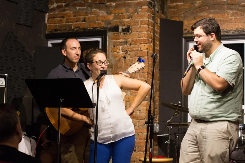 three people with microphones and guitar standing around