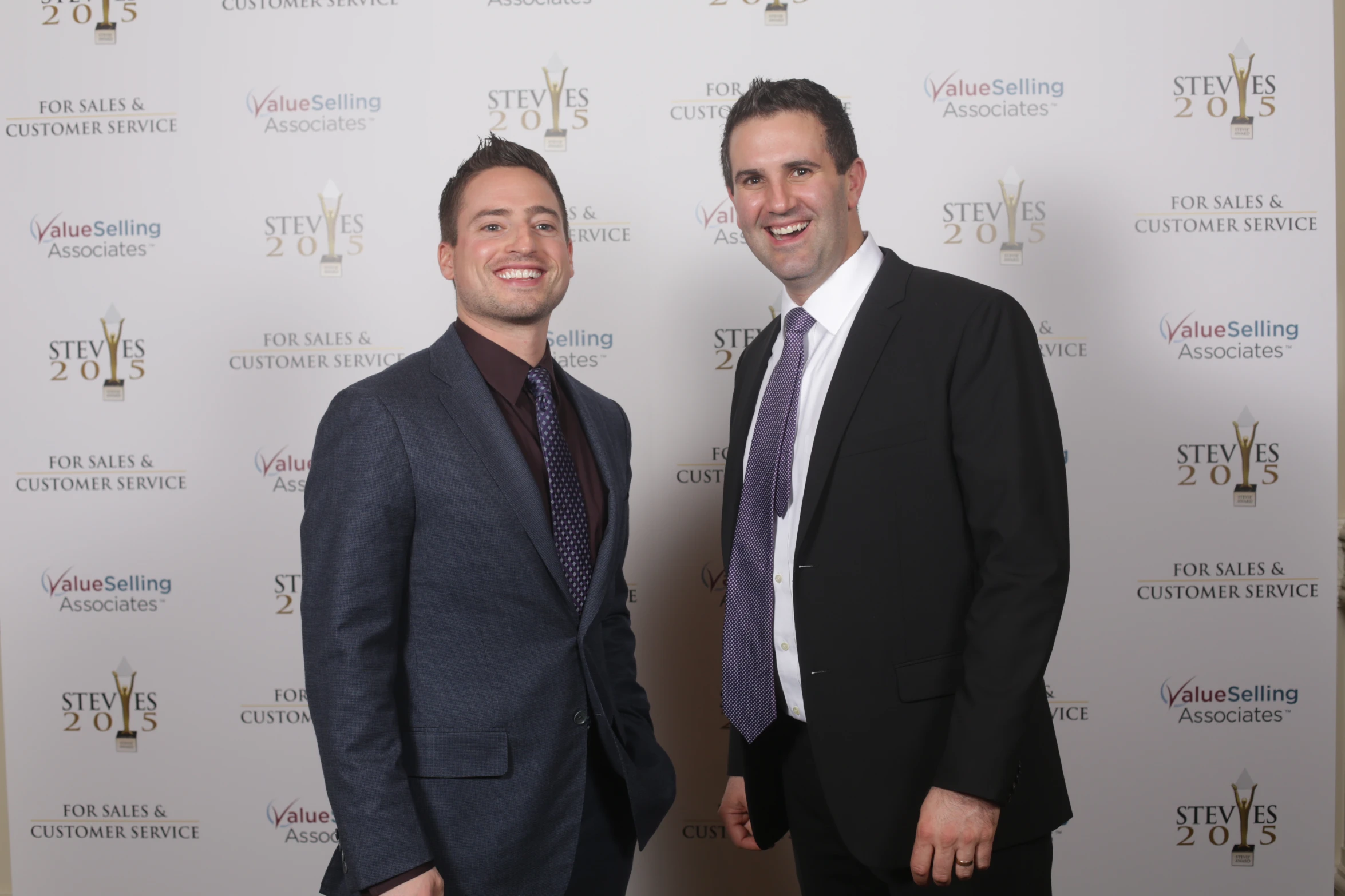 two men in suit and tie standing together on a red carpet