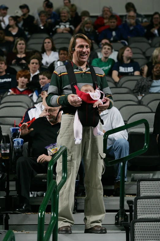 a man holds two babys while standing in front of a stadium crowd