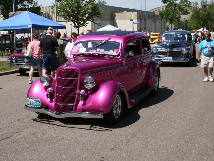 a pink car is parked near people and other vehicles