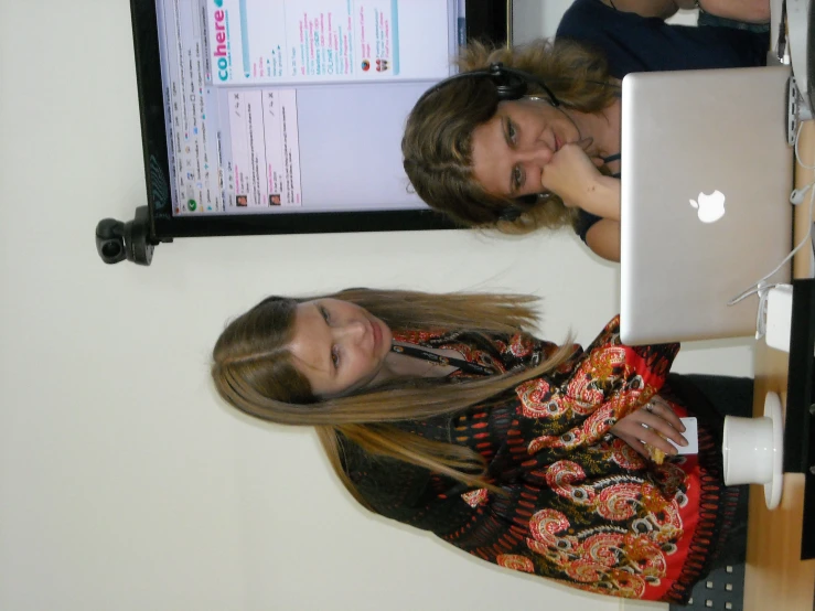 a girl leaning over a laptop while another person looks at her