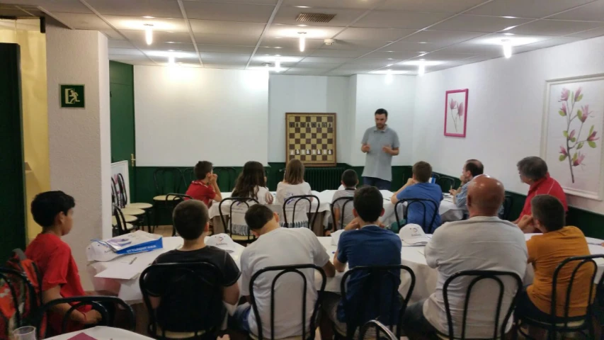 several people sit in the center of a room, listening to a man giving a presentation