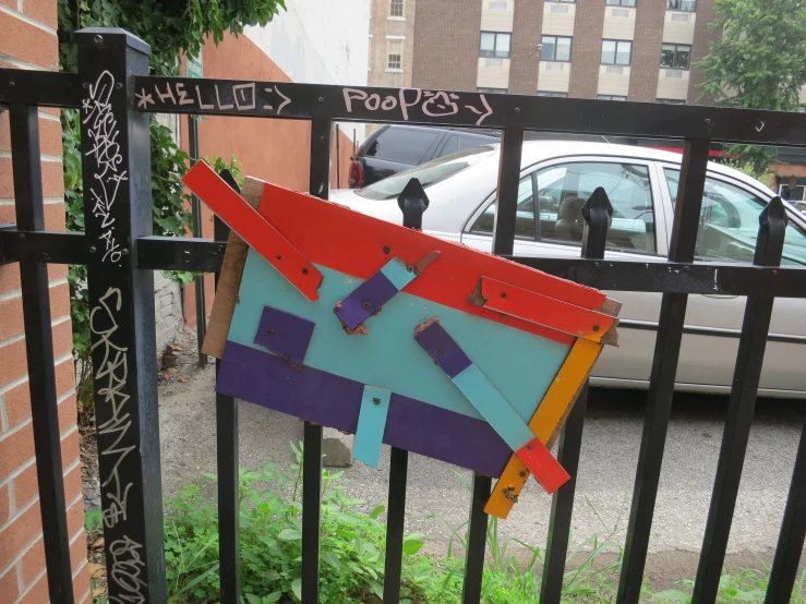 an orange and blue sculpture hanging on a fence