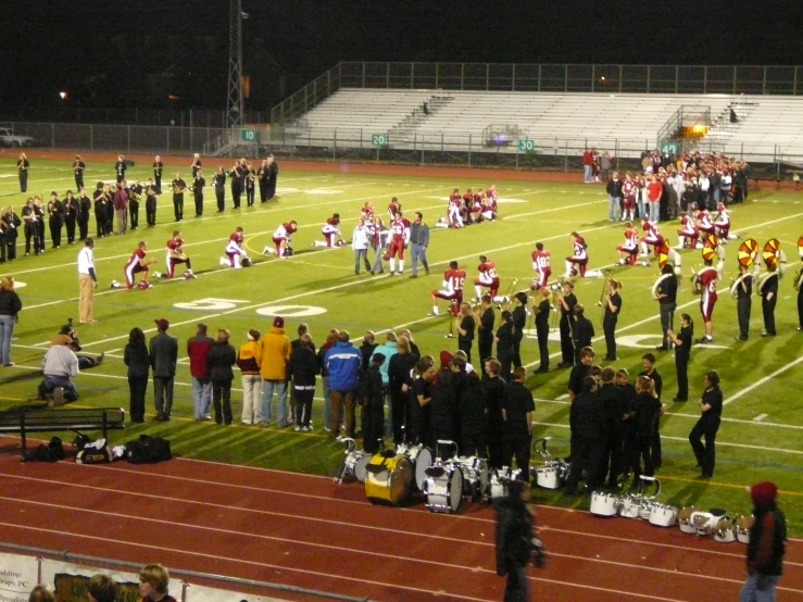 a band of marching musicians stand in line at the stadium on the sideline