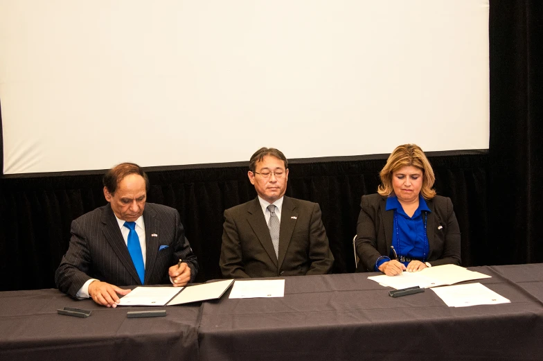 three people sitting at a table signing documents