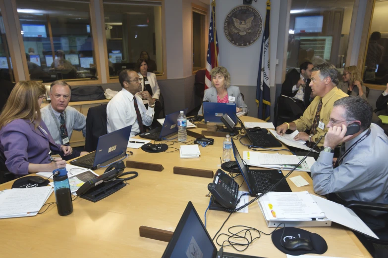 a group of people sitting around a conference table with laptop computers