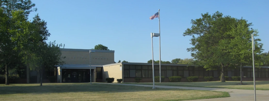 a clock tower stands near a school with an american flag waving