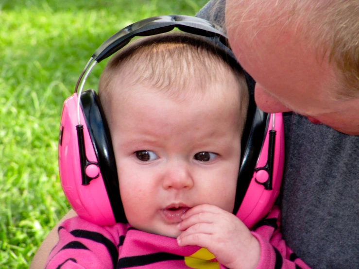 a young man holds his newborn daughter with headphones on