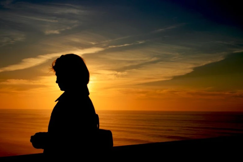 the silhouette of the person is shown at sunset by the water