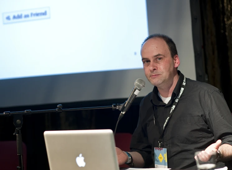 the man is sitting in front of a microphone and speaking into a laptop computer