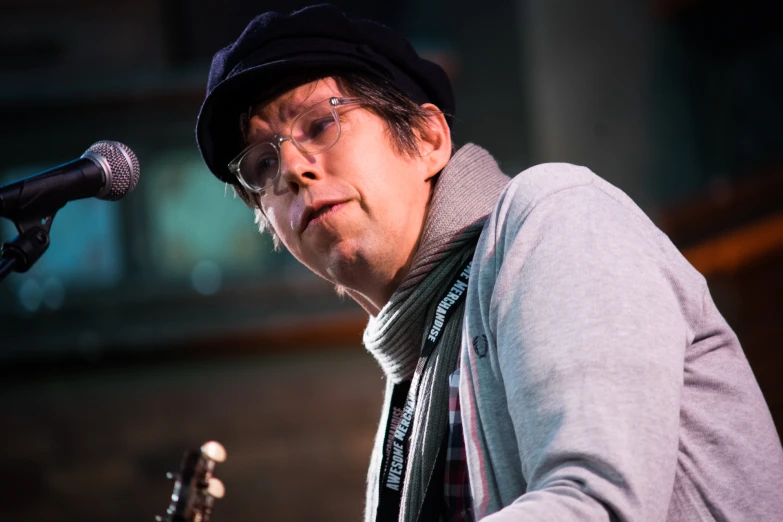 a man with glasses and a black hat standing by a microphone